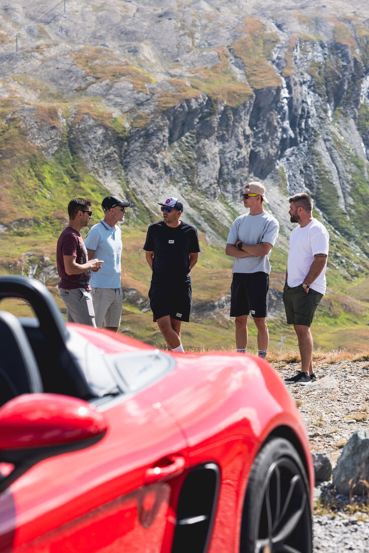 Pause unterhalb der Felswand, im Vordergrund ein roter Porsche